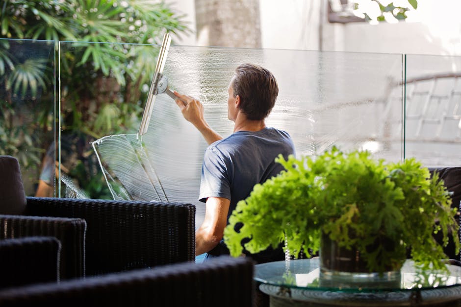 Residential Window Washing Near You in Lake Martin - A man cleaning a glass barrier outdoors with a squeegee, surrounded by greenery.