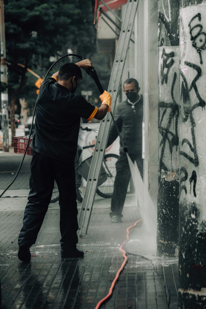 pexels-photo-10133570-10133570 Workers cleaning graffiti off city building facade with a pressure hose.