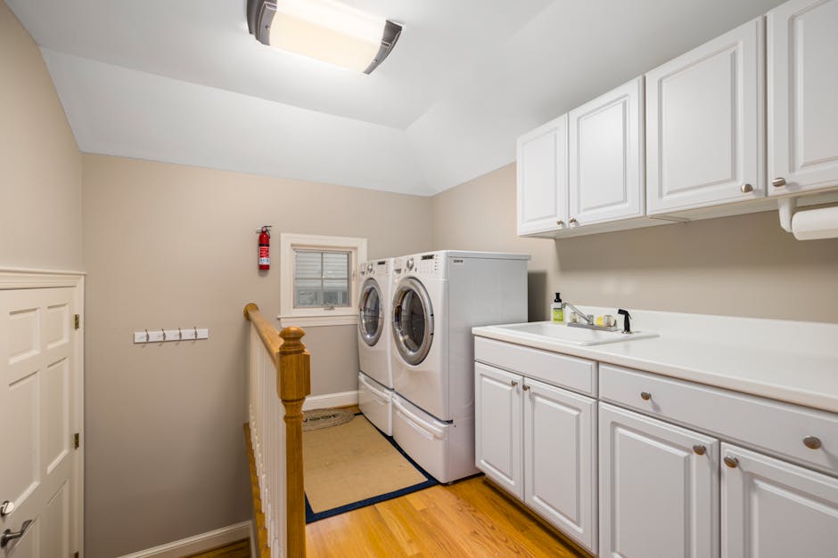 pexels-photo-8186483-8186483 Spacious and clean laundry room featuring modern appliances and white cabinetry.
